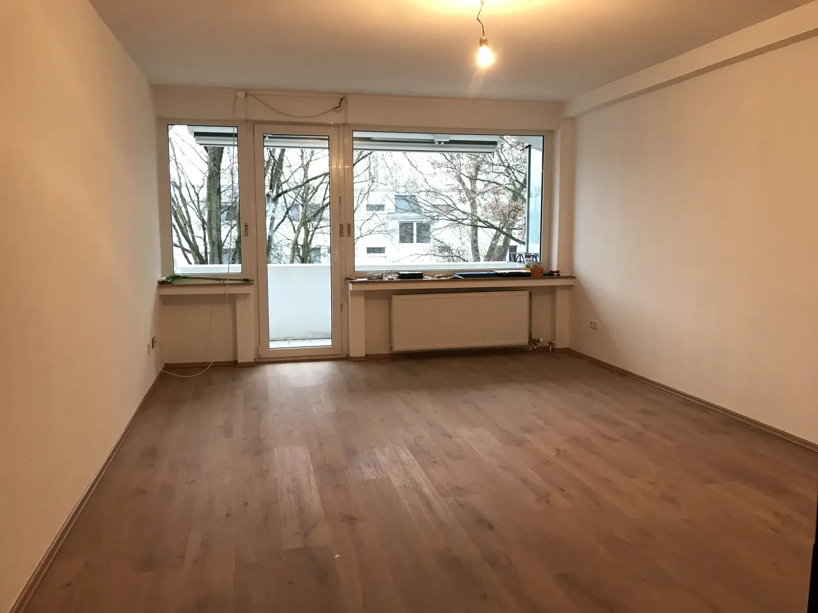 Wohnzimmer mit großer Fensterfront, Balkontür und Laminatboden in Holzoptik